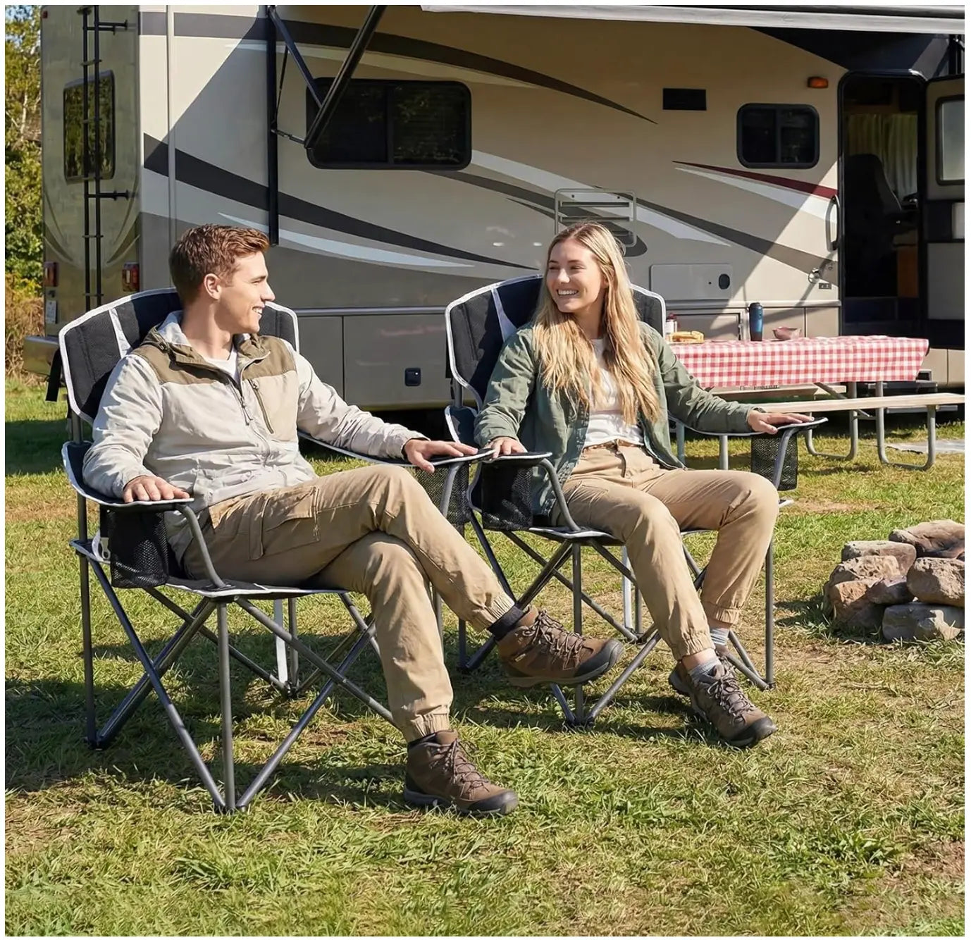 Two people sitting in camping chairs in front of a large RV.