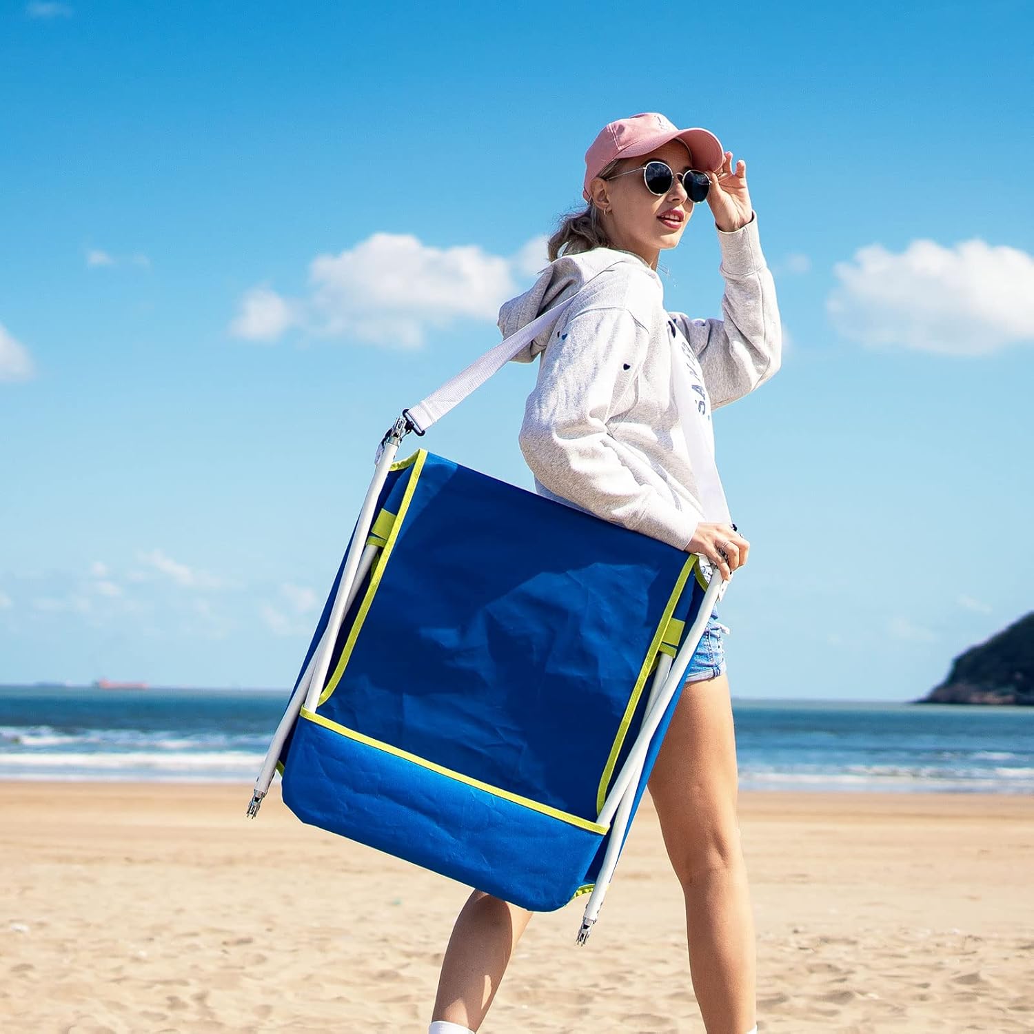 Woman holding a blue beach chair on a sandy beach with ocean view