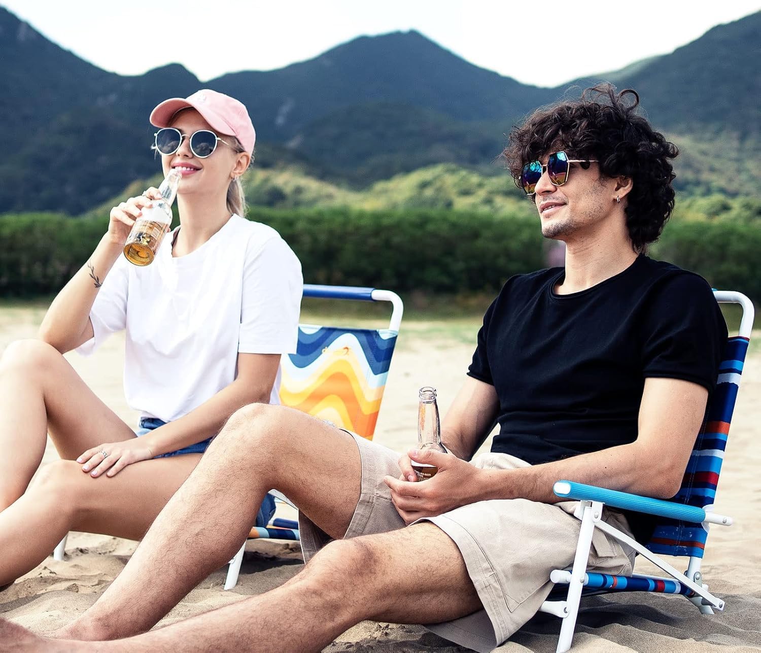 Two people sitting on beach chairs with mountains in the background