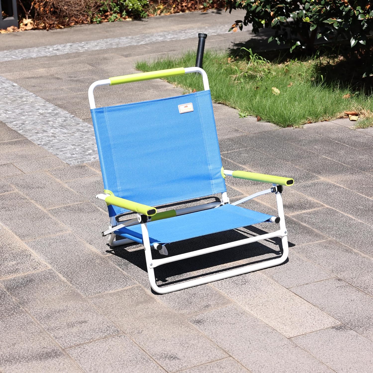 Blue folding chair with green armrests on a paved surface