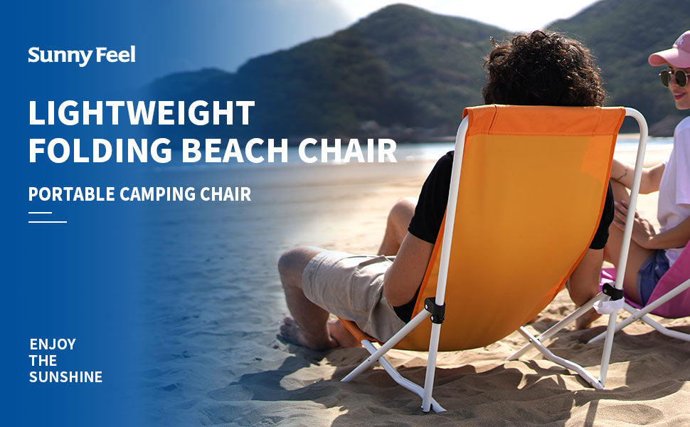 Person sitting on a Sunny Feel lightweight folding beach chair at the beach with mountains in the background.