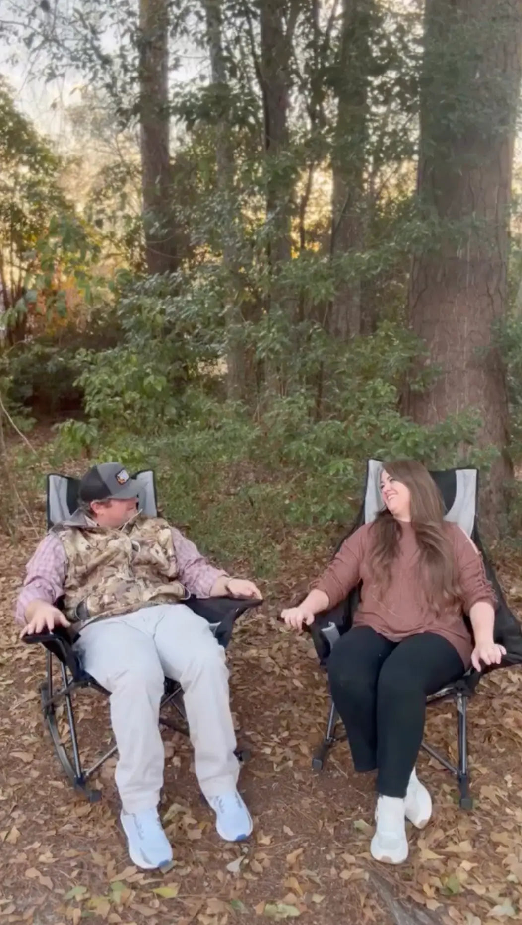 Two people sitting in folding chairs in a forest setting