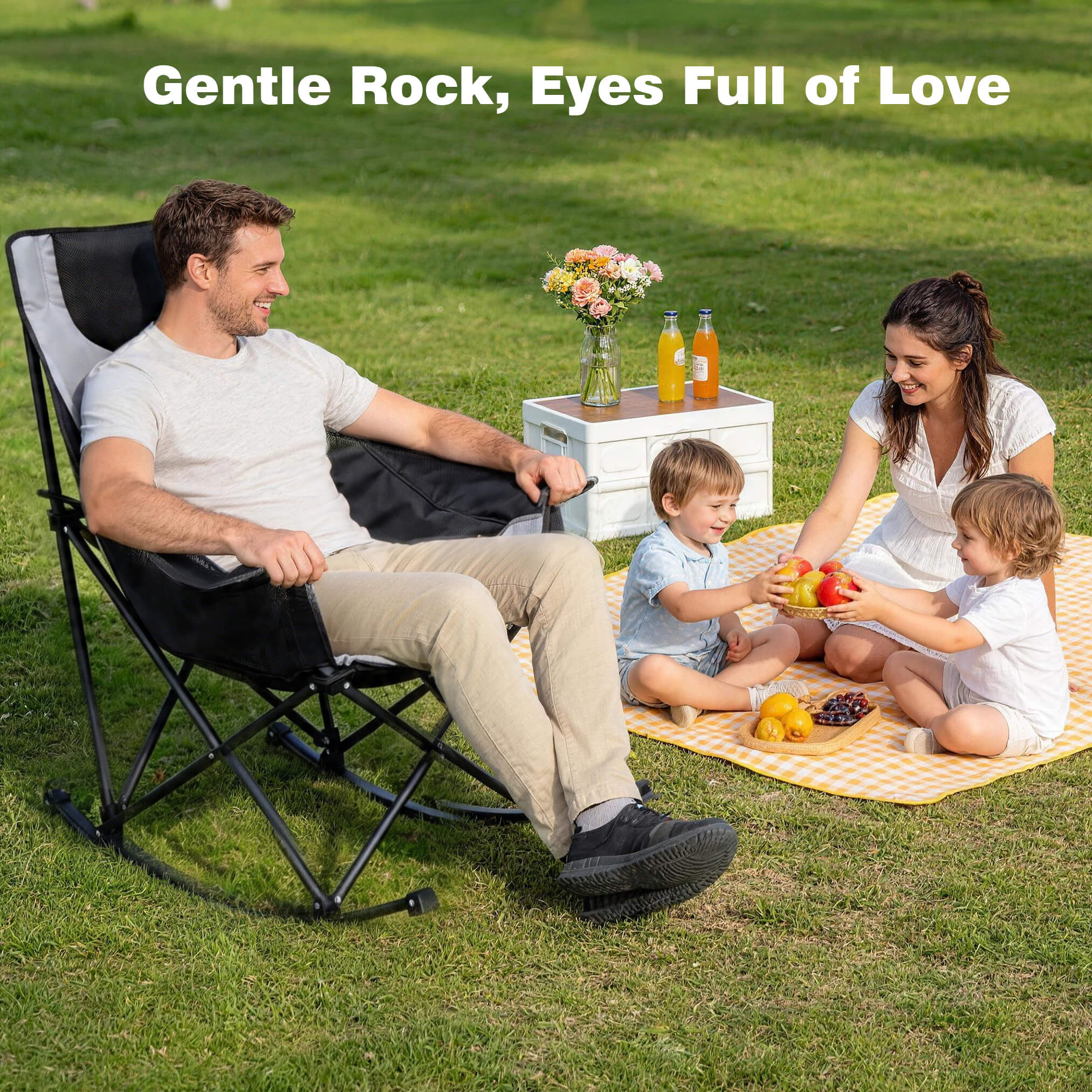 Family enjoying a picnic on a grassy field with a man in a black chair, woman, and two children.