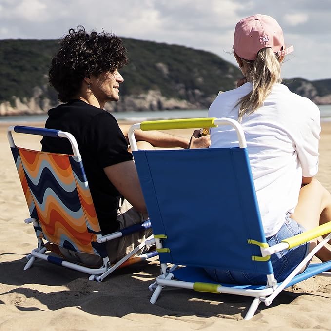 Two people sitting on colorful beach chairs at the beach with a scenic background.