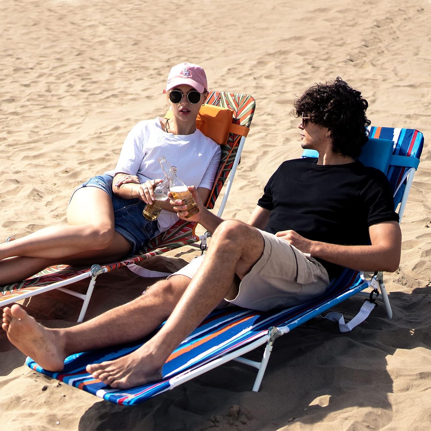 Two people sitting on beach chairs in the sand, enjoying drinks.