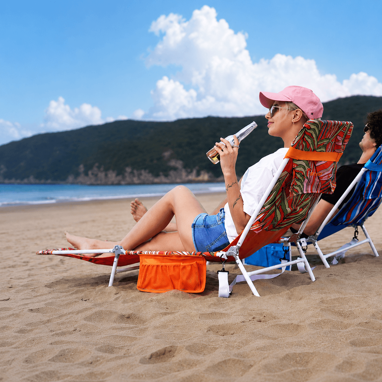 Two people relaxing on beach chairs with a scenic background of mountains and ocean.