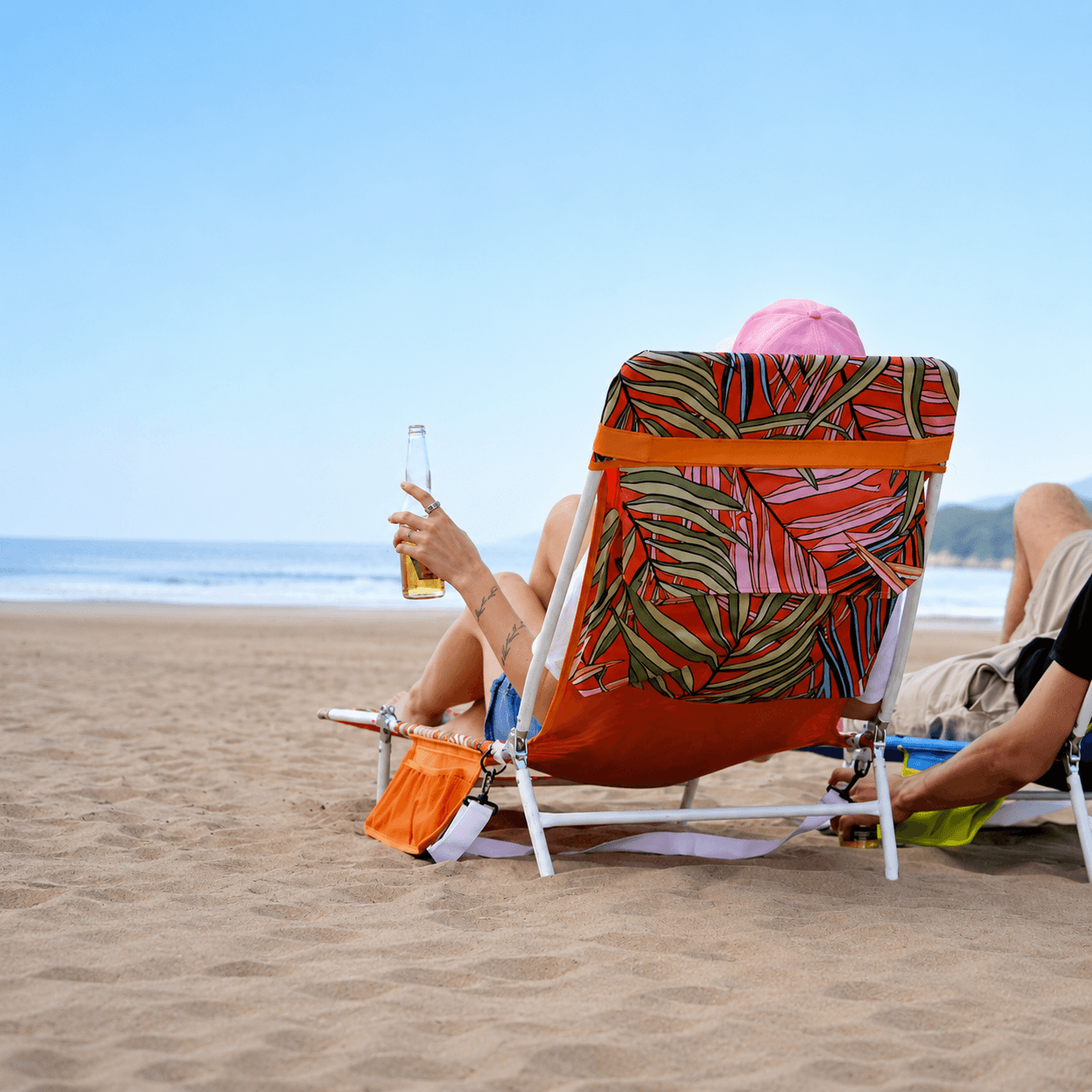 Person sitting on a colorful beach chair with a drink, enjoying a day at the beach.