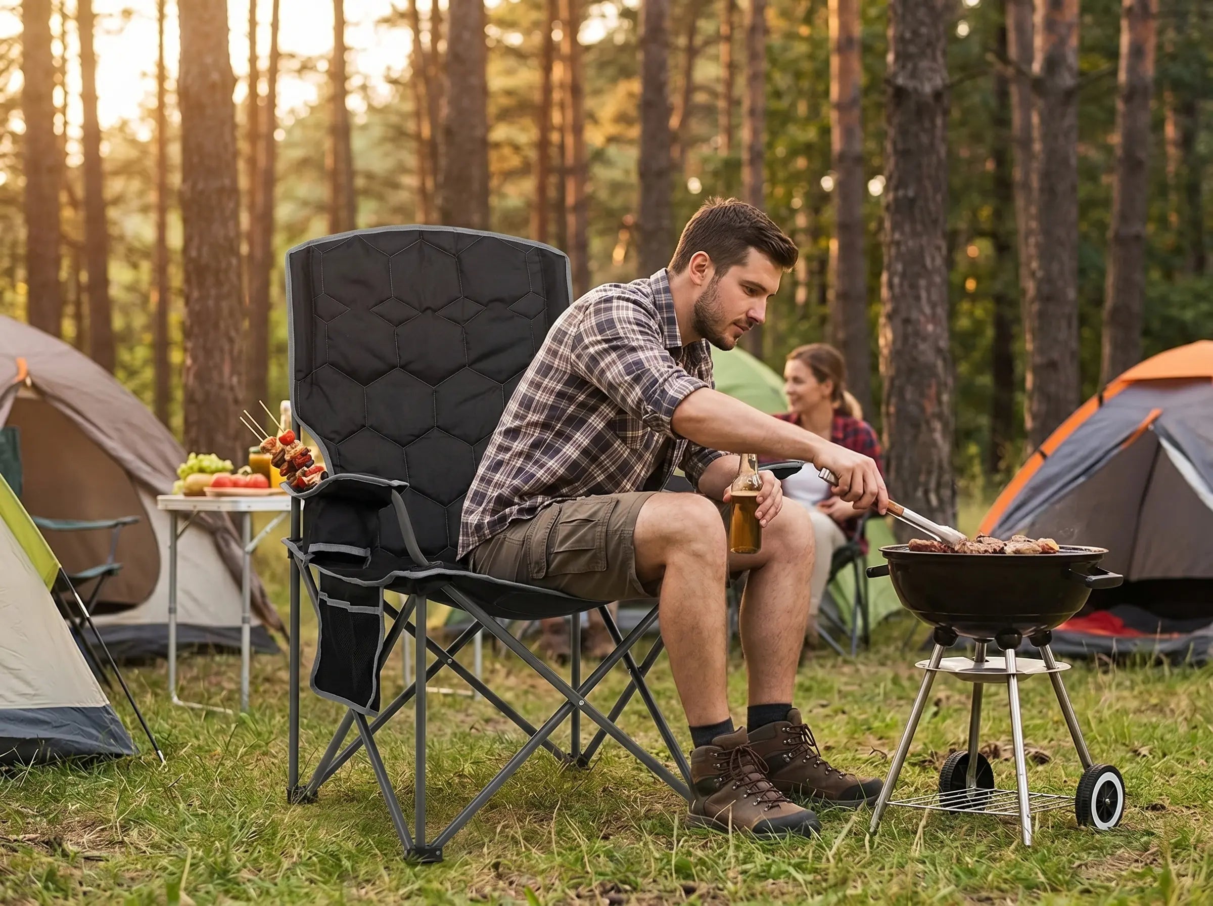 Man grilling outdoors in a camping setting with tents and trees in the background.