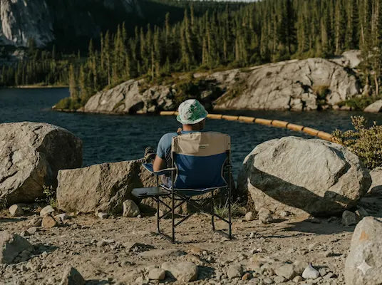Person sitting in a chair by a lake surrounded by rocks and trees