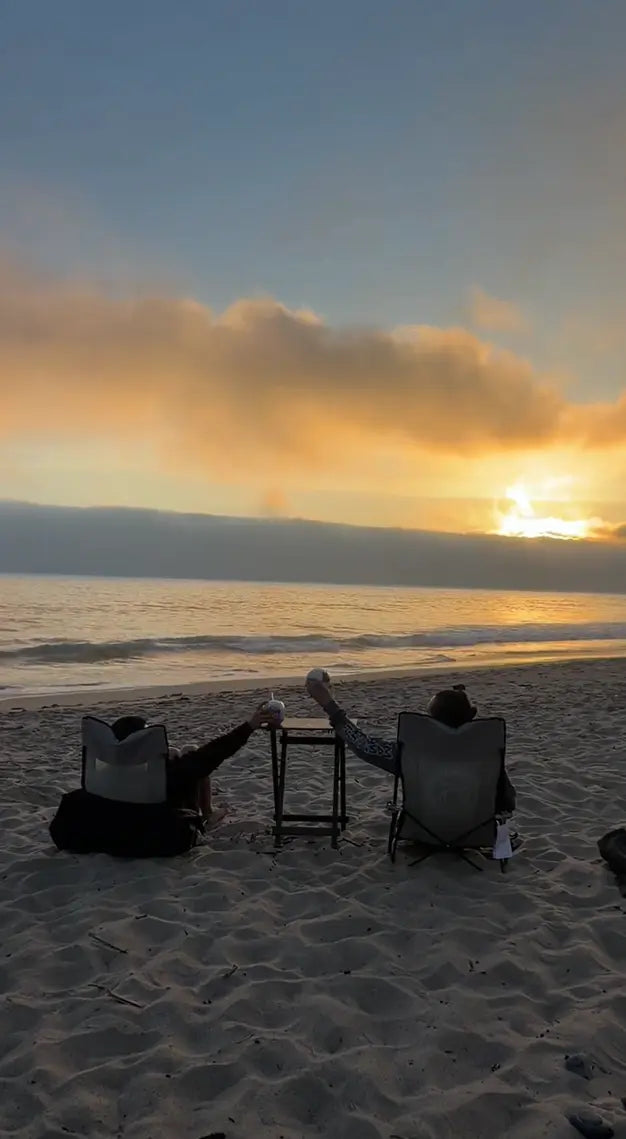 Two people sitting at a table on a beach during sunset.