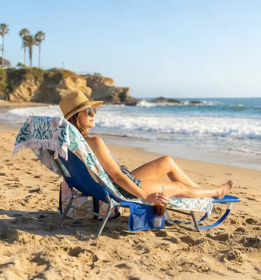 Woman relaxing on a beach chair with a towel draped over it, enjoying a sunny day at the beach.