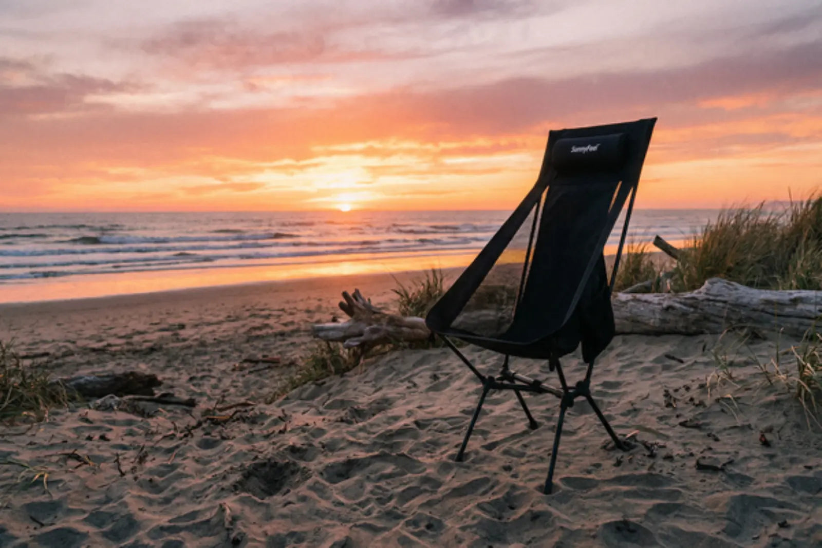 Black camping chair on a sandy beach with a sunset in the background