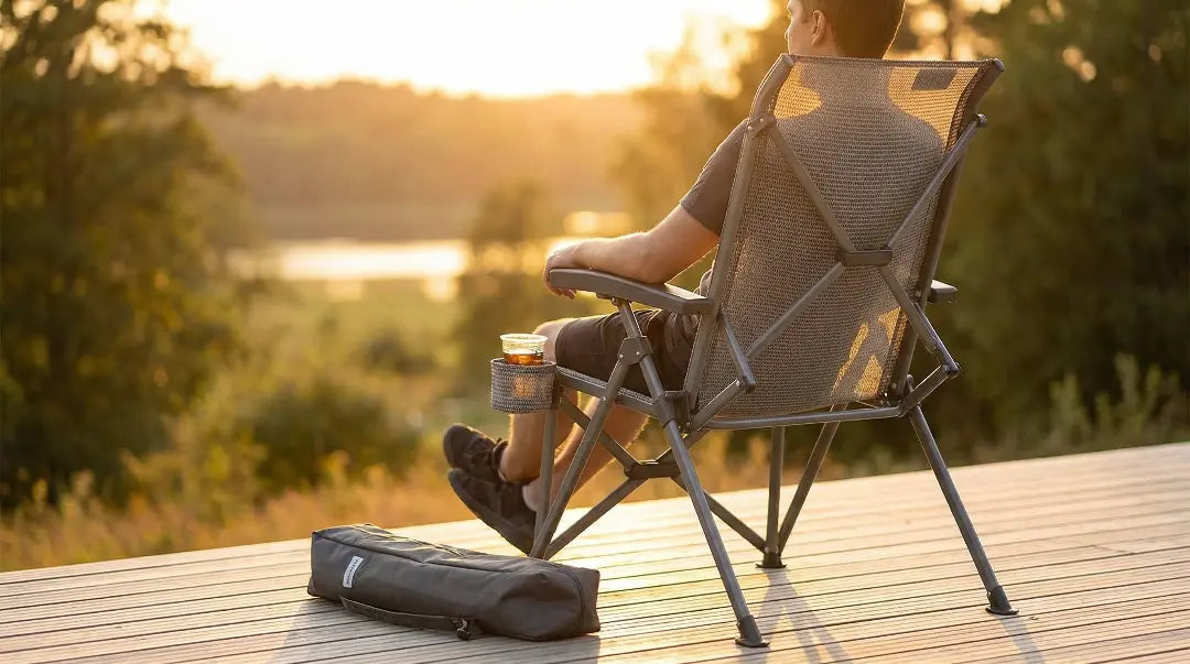 Person sitting in a folding chair by a lake at sunset