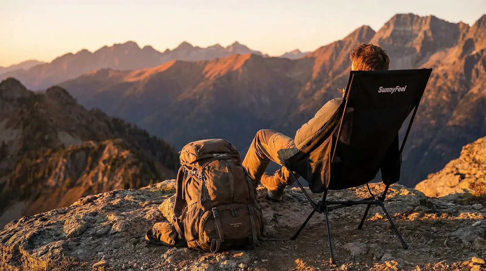 Person sitting in a folding chair enjoying a mountain view with a backpack nearby.