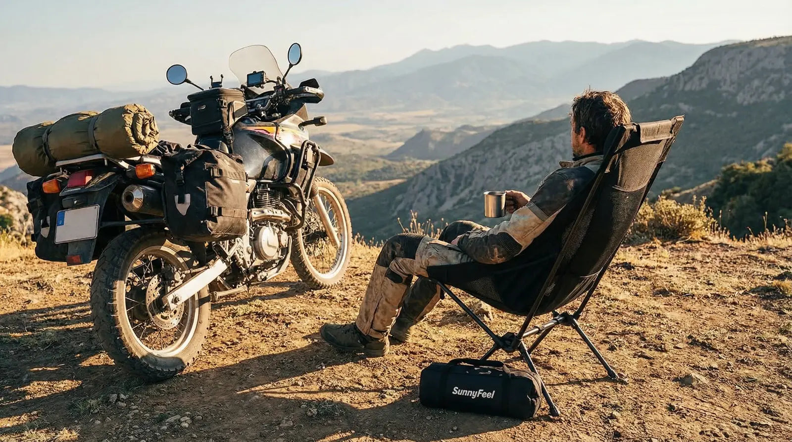Person sitting in a chair next to a motorcycle with a scenic mountain view.